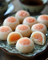 Traditional Asian pastries filled with sweet orange yolk cream on decorative plate. Close-up view shows delicate white mochi exterior and vibrant filling.
