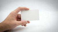 Male hand holding blank white business card mockup against neutral background for branding and corporate identity design projects.