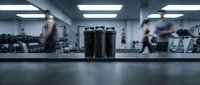 Modern fitness gym interior with protein shake bottles on counter, blurred people exercising with weights and equipment in background for health lifestyle.