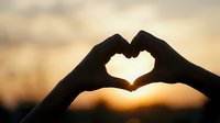 Silhouette of hands forming a heart shape against a warm golden sunset sky, symbolizing love, romance, and togetherness.