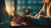 Young woman typing on laptop computer in warm evening light with cozy sweater, working from home or cafe atmosphere for productivity and technology concepts.