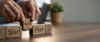 Businessman hands arranging wooden blocks spelling Start Work Plan on desk, representing business strategy and project management planning process.