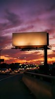 Blank billboard against dramatic purple sunset sky over busy highway with traffic lights creating urban advertising space for marketing campaigns.