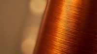 Copper wire spool with metallic orange sheen in warm lighting. Industrial electrical component for manufacturing, electronics and construction projects.