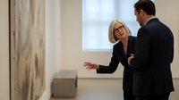 Professional blonde businesswoman in glasses presenting to male colleague in modern office meeting room discussing corporate strategy and collaboration.