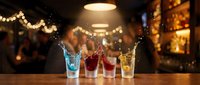 Colorful cocktail shots with splashing liquid on wooden bar counter in warm ambient restaurant lighting for nightlife entertainment.