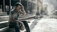 Exhausted male construction worker sitting on rubble at demolition site, holding hard hat, stressed and tired after hard labor day.