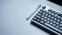 Mechanical keyboard with stylus pen on white surface, workspace setup for typing and design work.