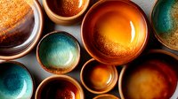 Handcrafted ceramic bowls in vibrant turquoise and amber colors arranged on gray surface, showing artistic glazing technique with metallic and gradient effects.