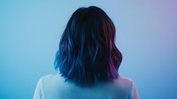 Young Asian woman with blue dyed hair shown from behind in neon lighting with gradient from blue to purple creating mysterious atmospheric mood.