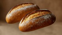 Two freshly baked artisan bread loaves with golden brown crusts and flour dusting on warm wooden surface for bakery and food photography.