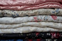 Stack of vintage floral quilts and comforters in soft pastel colors creating cozy layered bedding display for home decor and textile design projects.