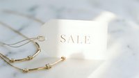 Elegant sale tag on marble surface with gold jewelry necklace, luxury retail discount concept for fashion and jewelry promotions.