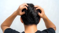 Asian man scratching head from behind view showing scalp irritation, dandruff problem and itchy sensation on white background, health and haircare concept.