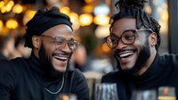 Two and beards sharing genuine laughter at cafe table, warm bokeh background creates intimate atmosphere.
