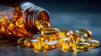 Golden omega-3 fish oil capsules spilling from amber glass bottle on wooden surface. Dietary supplements for health and wellness nutrition concept.