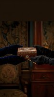Hands in black gloves carefully handling ornate wooden jewelry box in vintage interior setting with warm atmospheric lighting.