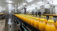 Orange juice bottles moving on automated conveyor belt in modern beverage production facility with stainless steel equipment for commercial manufacturing.