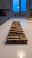 Row of rustic wooden clothespins lined up on a marble kitchen counter with a blurred window background creating depth.