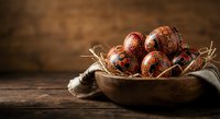 Traditional painted Easter eggs in rustic wooden bowl on vintage table with burlap cloth creating warm holiday atmosphere for seasonal celebrations.