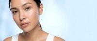 Young Asian woman with natural makeup and glowing skin applying white cream dots on face for skincare routine against clean white background.