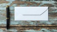 White envelope and black luxury pen on rustic turquoise wooden table background. Business communication concept for correspondence and mail.