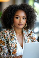 Young African American businesswoman with curly hair working on laptop in modern office environment for professional corporate marketing materials.