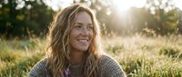 Happy blonde woman with wavy hair smiling outdoors in golden sunlight wearing cozy sweater in natural field setting for lifestyle and wellness content.