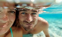 Couple taking underwater selfie in crystal clear turquoise water during summer vacation, showing joyful expressions and natural light reflections.
