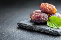 Fresh dates with green leaf on dark slate stone surface for healthy snacking and Middle Eastern cuisine preparation.