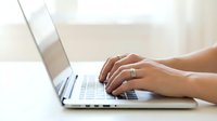 Female hands typing on modern silver laptop computer keyboard in bright office workspace for business productivity and remote work applications.