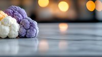 Fresh colorful cauliflower heads in white, orange and purple varieties arranged on marble surface with soft bokeh lights in background for healthy eating concept.
