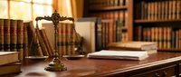 Brass scales of justice on wooden desk in law library with legal books for attorney office, courtroom, legal services, and judicial system concepts.