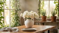 White roses in ceramic vase on wooden table near sunny window with plants. Cozy home interior design for kitchen dining room decor and floral arrangements.