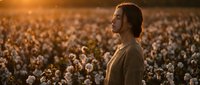 Young Caucasian man standing peacefully in cotton field during golden hour sunset, agricultural farming concept for rural lifestyle content.