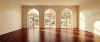 Empty luxury room with dark hardwood floors and three arched French doors leading to garden patio. Warm natural lighting creates elegant interior space.