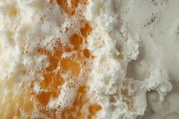 Macro shot of white foamy soap bubbles and orange liquid creating abstract texture pattern with contrasting colors and organic shapes for bathroom or cleaning concept.