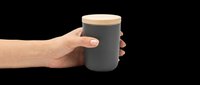 Hand holding dark gray ceramic jar with wooden lid, isolated on transparent background. Ready for design use on product mockups, packaging designs, e-commerce graphics, and promotional materials.