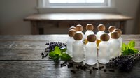 Essential oil bottles with wooden caps arranged on rustic table with lavender sprigs and mint leaves for aromatherapy and natural wellness products.