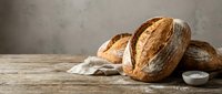 Fresh artisan bread loaves with golden crust on rustic wooden table with linen cloth, perfect for bakery marketing and food photography projects.