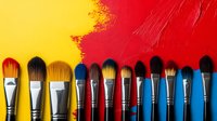 Paint brushes arranged in row on vibrant red and yellow background, showing variety of sizes and bristle types for artistic and creative projects.