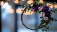 Romantic floral hoop wreath with pink roses and purple flowers on blurred bokeh background, modern wedding decoration for ceremony arch and venue styling.
