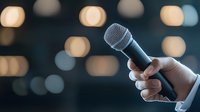 Professional holding dynamic microphone against blurred bokeh lights background, capturing live performance atmosphere for public speaking and entertainment events.