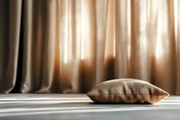 Beige linen pillow on wooden floor with soft natural light filtering through draped curtains, suitable for home decor and interior design projects.