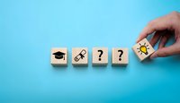 Hand placing wooden blocks with education symbols graduation cap key question marks and lightbulb on blue background representing learning process and knowledge development.