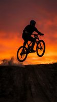 Mountain biker silhouette jumping against dramatic orange sunset sky. Extreme sports adventure and outdoor recreation concept for active lifestyle designs.