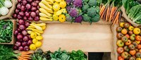 Wooden cutting board surrounded by fresh organic vegetables including red onions, yellow peppers, purple cabbage, carrots, tomatoes and leafy greens. Flat lay overhead view with copy space for food, cooking or healthy eating content.