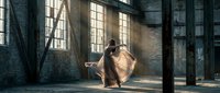 Young woman dancer performing contemporary dance in abandoned industrial warehouse with dramatic sunlight streaming through large windows creating atmospheric mood.