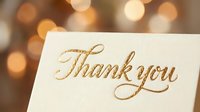 Thank you card with gold script lettering on cream background, blurred golden bokeh lights behind. Suitable for gratitude, appreciation, greeting cards, invitations.