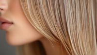 Close-up profile view of young caucasian woman with straight blonde hair showing partial face, lips and hair texture against blurred background.